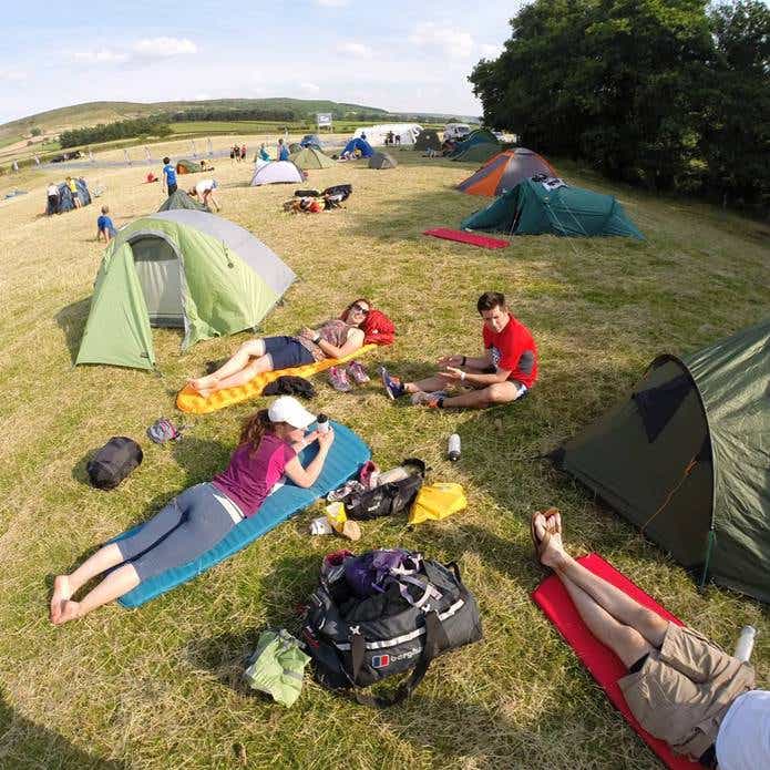 キャンプ場のテントの外で寝そべりくつろぐ人たち