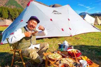 テントをバックにキャンプで料理を食べる男性