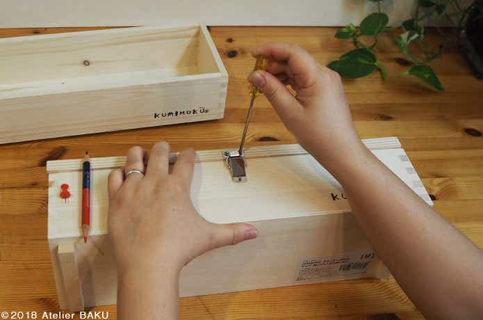 木製BOXに金具を留める手、ドライバー、色鉛筆、画鋲