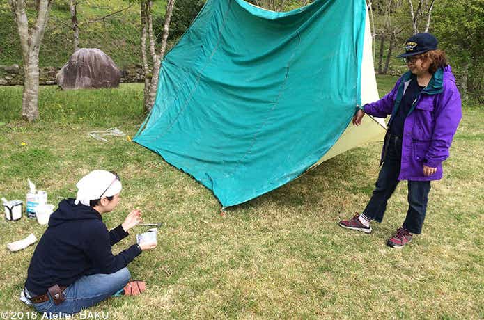 裏返したテント、防水液を塗る2人