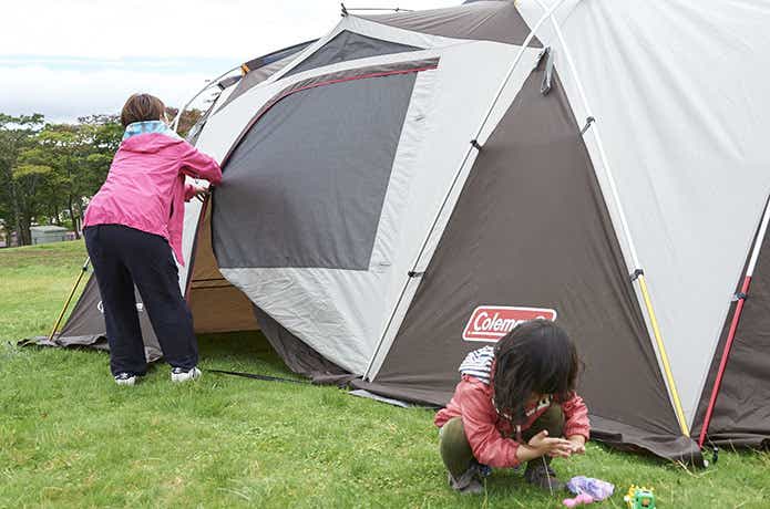 テントを設営する人とその前で遊ぶ子供