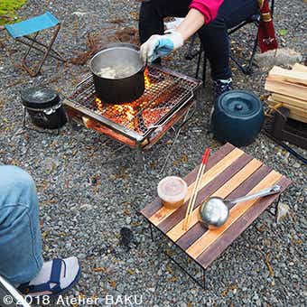 テーブル、おたま、菜箸、焚き火台、鍋、料理する人