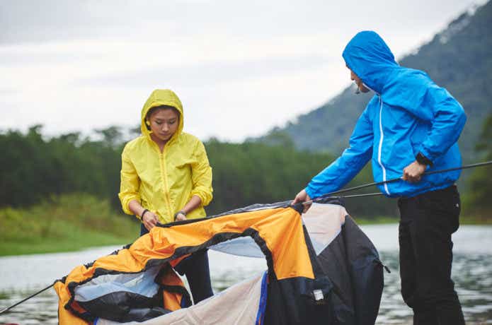 レインウェアを着て雨の中テントを組み立てる男女