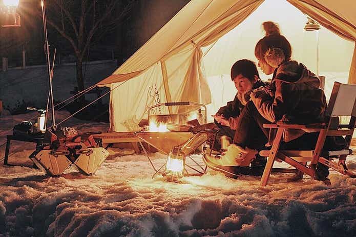テントの前の焚き火で暖を取る家族