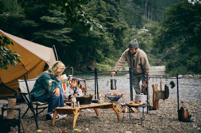 川辺でキャンプをしながら料理をしている家族