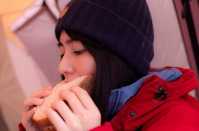 キャンプで食パンを食べる女性