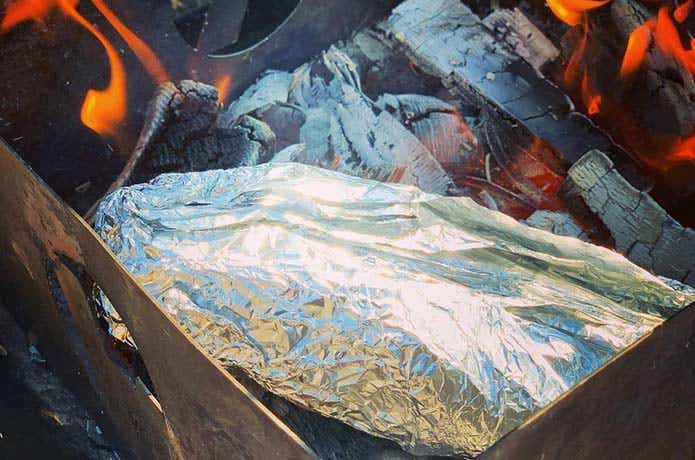 アルミホイルで包んだ豚肉を熾火状態の焚き火の中へ入れた様子