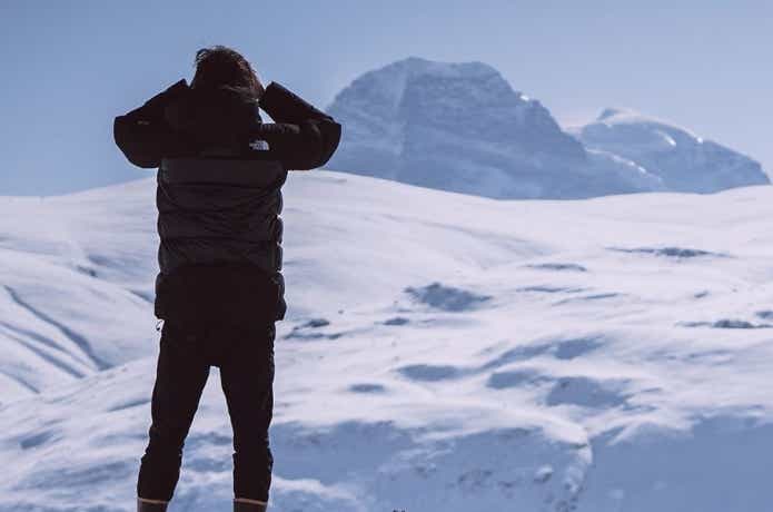 ザ・ノース・フェイスのアウターを身に着け雪原に立つ男性