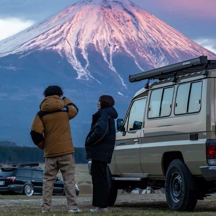 アウトドアウェアを着てSUVの隣で富士山を見る男女