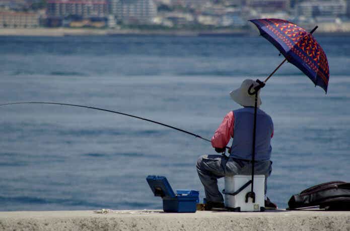 クーラーボックスに座って釣りをする人