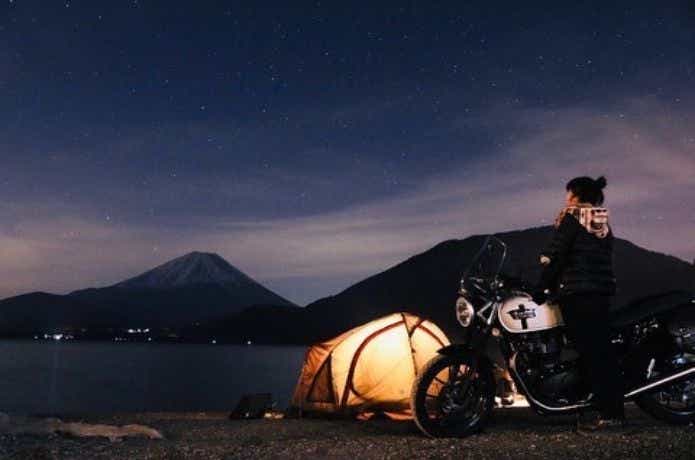 テントの近くでバイクに乗って夜空を眺める女性