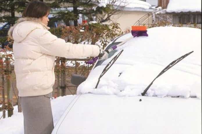 スノーブラシで車の雪かきをする女性