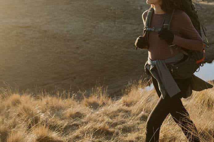 メリノウールの服を着て水辺の草原をハイキングする女性