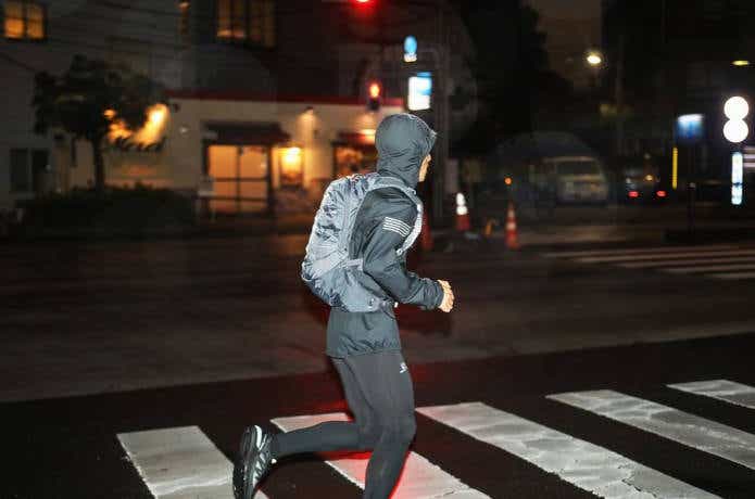 ランニング用バックパックを背負って夜の街中を走る男性
