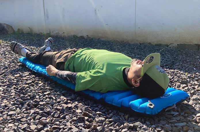砂利に敷いたモンベル「U.L. コンフォートシステムエアパッド 180」の上に寝る人