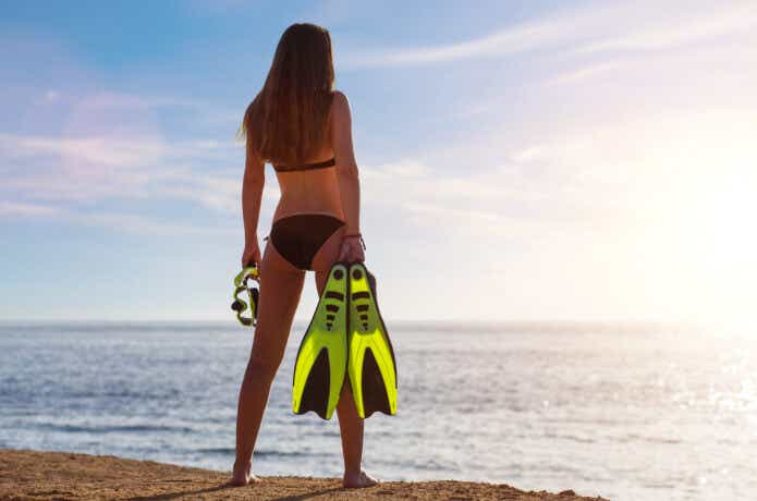 シュノーケルセットを持って砂浜に立つ女性