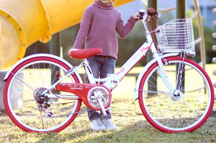 赤と白のジュニア向け自転車の横に立つ女の子