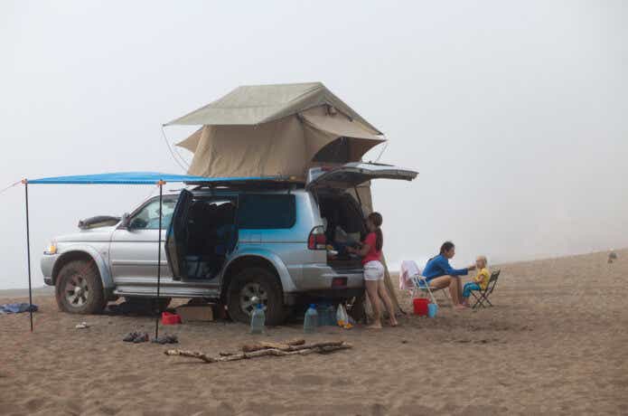 砂浜でルーフテントでくつろぐ家族