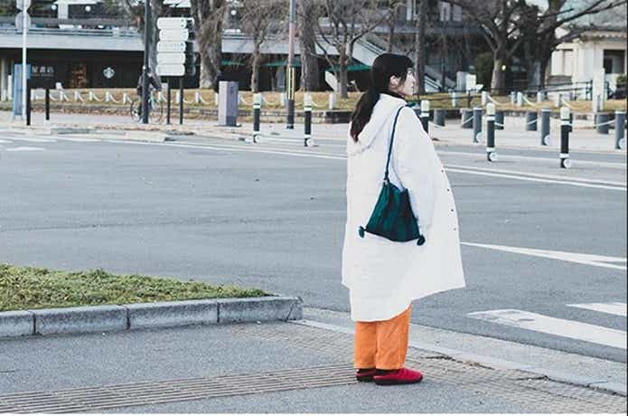 白いコートとオレンジのパンツと赤いSUBUのサンダルを身に着けた女性