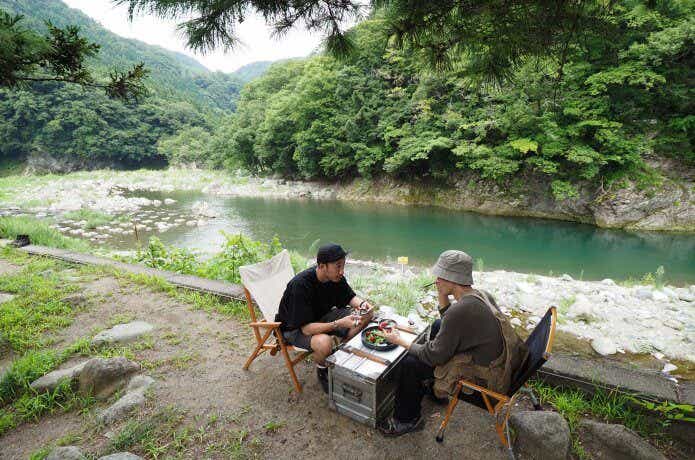 川沿いのキャンプ場で釣りキャンプ料理を楽しむ2人