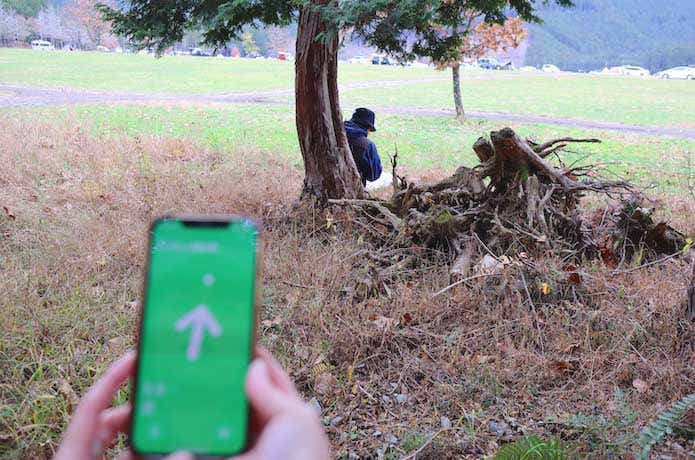 林の西端で目視できた迷子役と探すアプリ緑矢印画面表示したスマホ手元