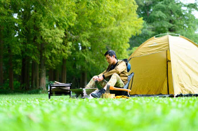 芝生のキャンプ場でソロキャンプをしている男性。