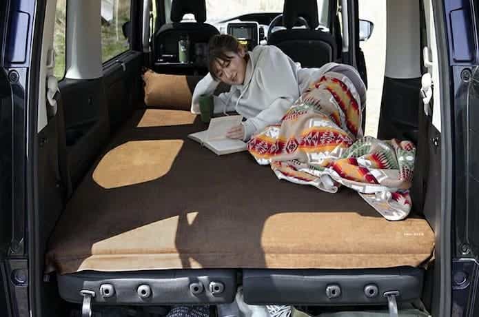 車中泊マットの上に寝て読書をしている女性