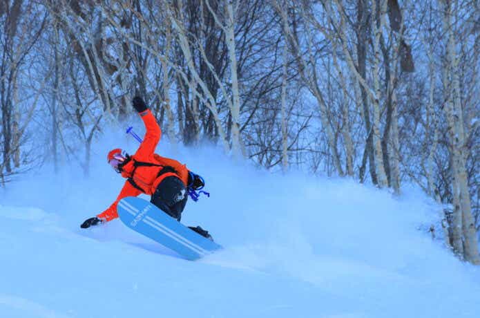 パウダーロッカーのスノボ板で新雪を滑っている男性