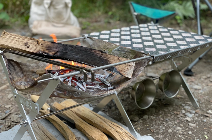 薪が入った焚き火台とテーブルとコップ