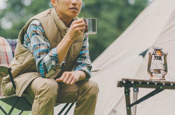 テントの前でマグカップでドリンクを飲む男性