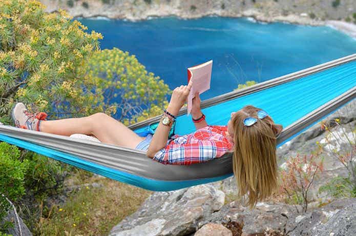 崖でナイロンの吊り下げ式ハンモックで本を読む女性