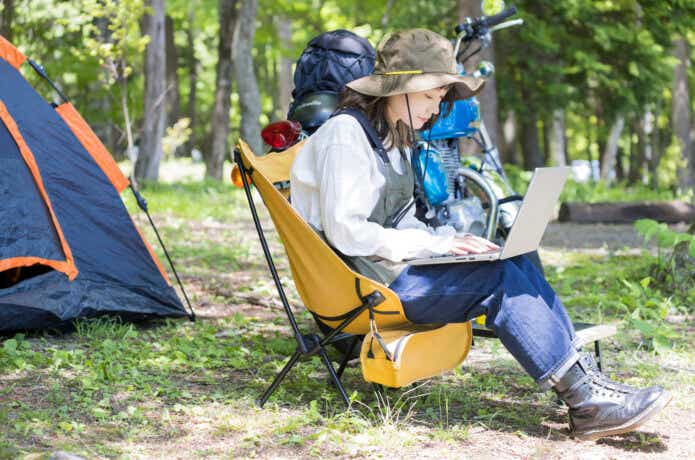 キャンプ椅子に座って仕事をする女性