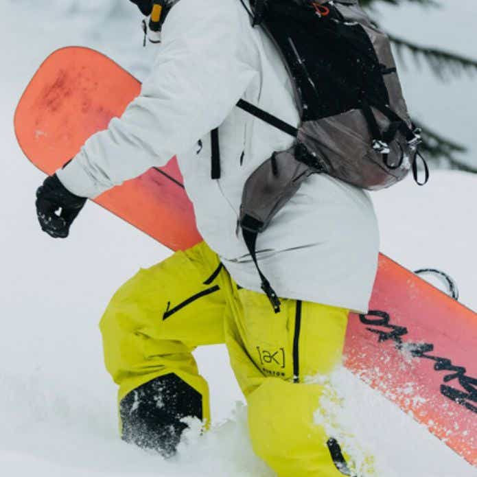 白のウェアと黄色いパンツを着て雪山を登る人