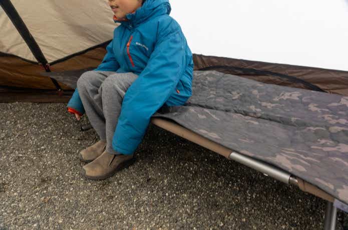 オレゴニアンキャンパーのアルミパディングマットを敷いたコットの上に座る男の子