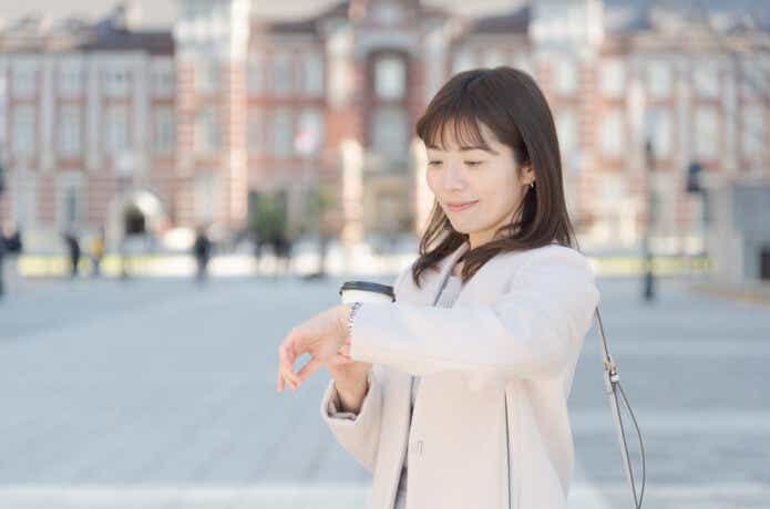 東京駅の前で腕時計をチェックする女性