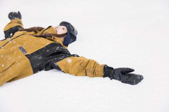 スノーボードグローブを装着して雪の上で仰向けになっている女性