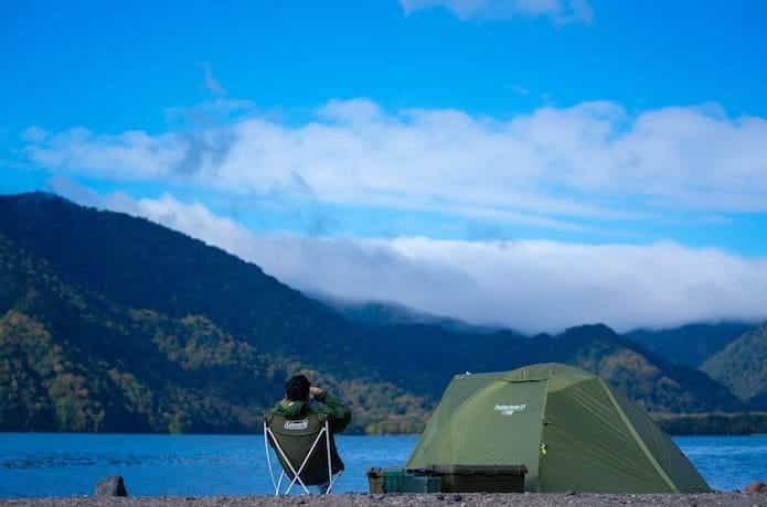 湖畔にテントを設営してソロキャンプを楽しんでいる男性