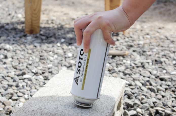 カセットボンベをコンクリートに押し付けてガスを抜いている