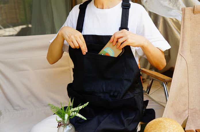 無印良品アウトドアエプロン着画女性、胸元のフラップポケットに携帯を出し入れする様子