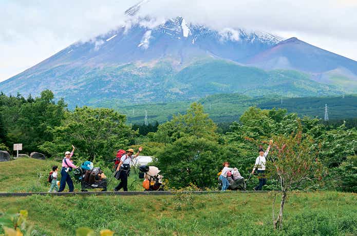 富士山をバックにキャンプギアを運びながら手を振る人々
