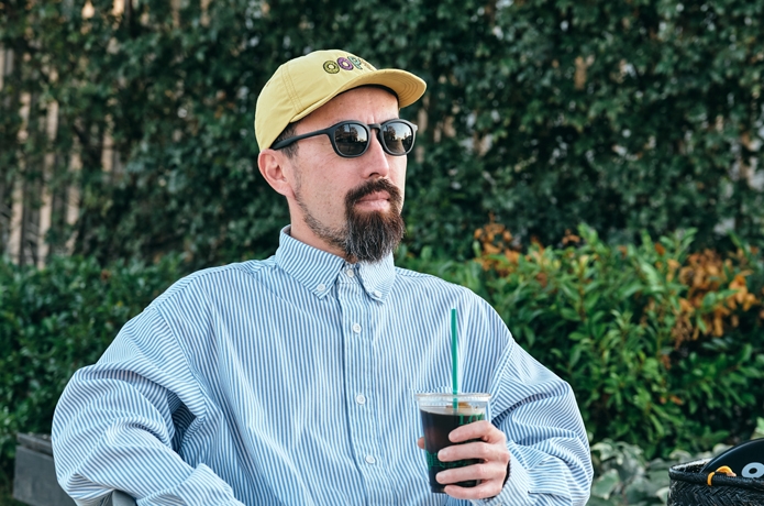 黒いサングラスをかけてコーヒーを片手に持ちストライプのシャツを着た男性