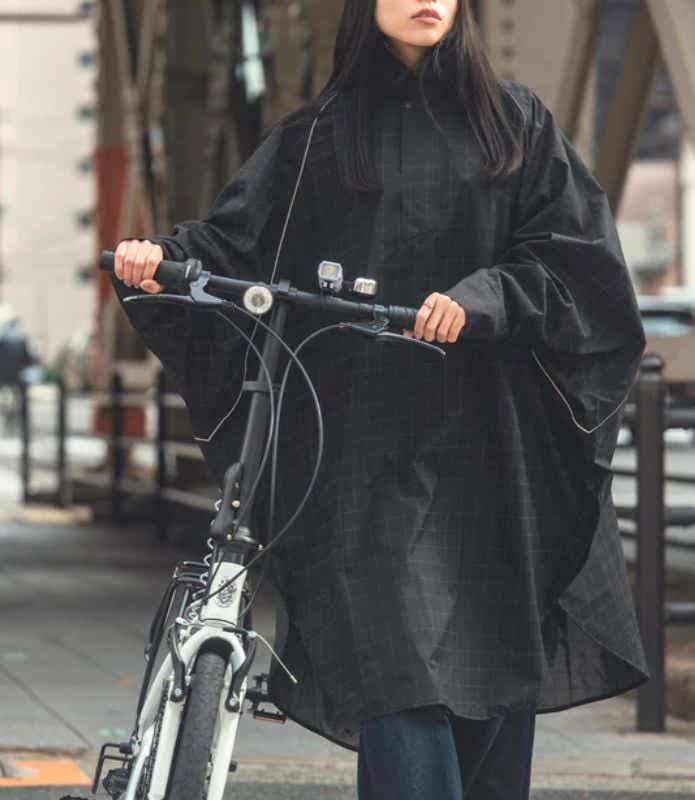 KIU「キウビジブルバイシクルレインポンチョ K407」を着て自転車を手押しする女性