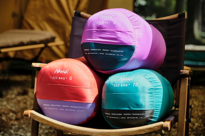 NANGAのピンク、赤、緑の寝袋が木製のキャンプチェアの上に乗っている写真