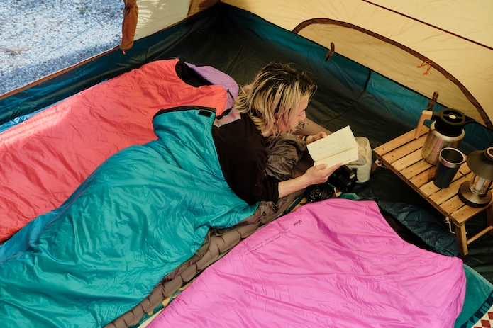 寝袋にくるまって本を読む男性