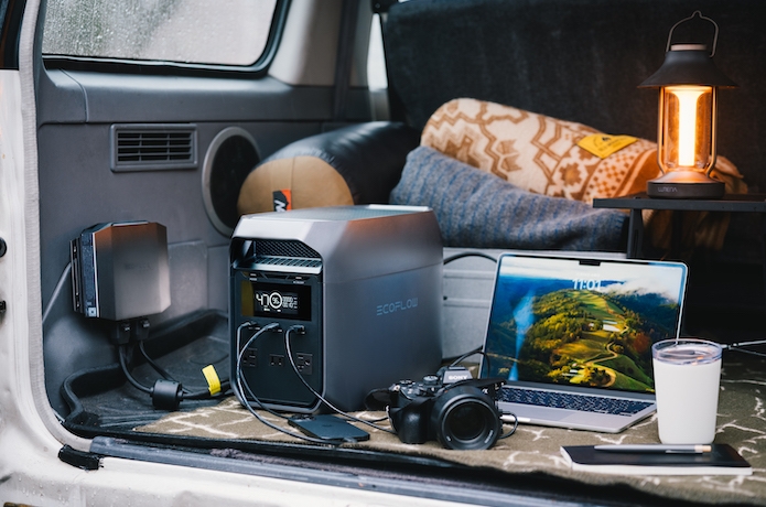 車の荷物スペースでポータブル電源からカメラとパソコンの充電をしている写真