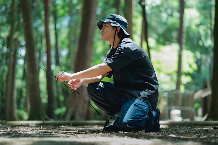 キャンプでテントの紐を調整している男性
