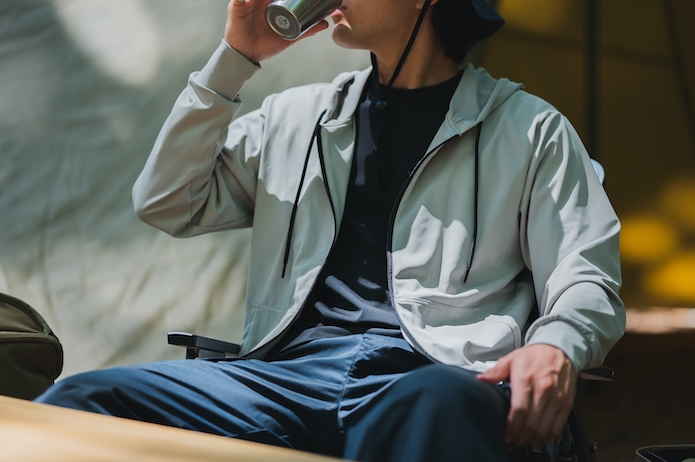 キャンプで白い上着を着て飲み物を飲んでいる男性