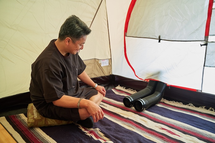 外から出ているダクトをテントの中で眺める男性