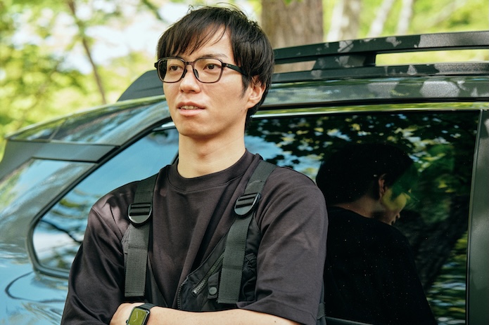 メガネをかけて車の前に立っている男性