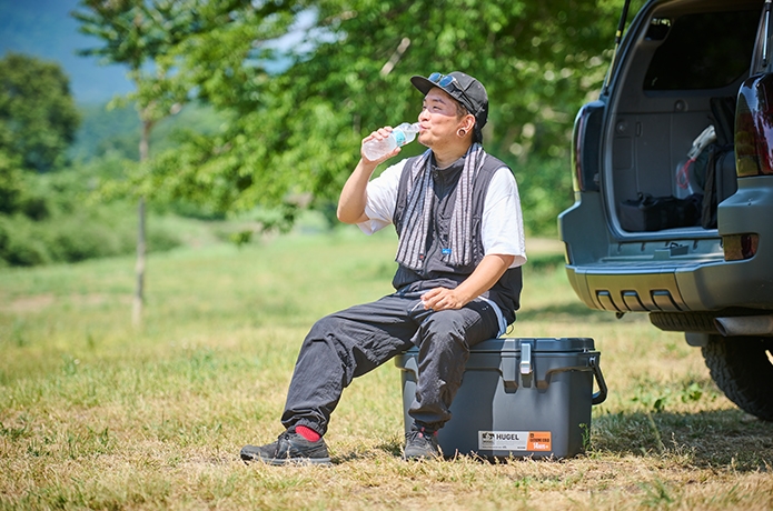 クーラーボックスに座って水を飲む男性